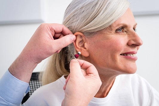 Seniorin bekommt ein modernes Hörgerät ins Ohr eingesetzt, Hörgeräte Anpassung Beratung.